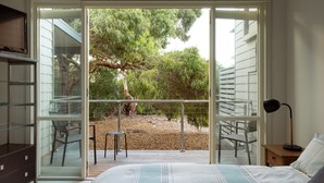 A bedroom with a large sliding glass door leading to a deck with outdoor furniture. - One Level at Broadbeach - Inverloch (Inverloch)