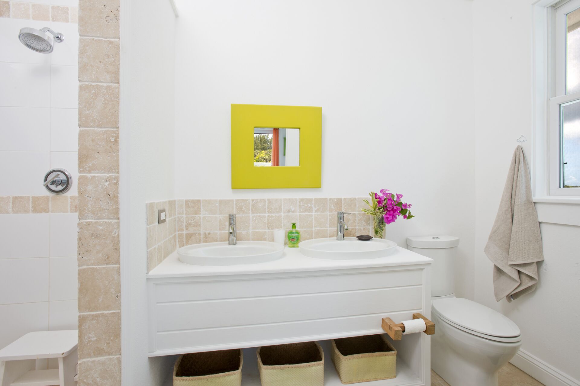 A bathroom with two sinks, a toilet, a shower, and a yellow-framed mirror.