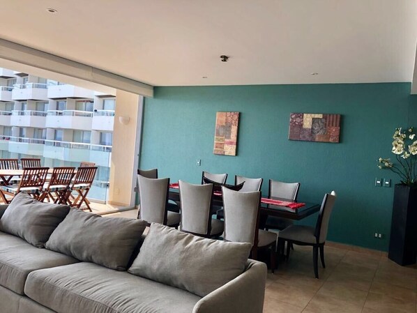 A modern living room with a sofa, dining table, and chairs. There are two artworks on the teal wall. - Amara Ixtapa, Luxury Oceanfront Condo, 6th Floor (Ixtapa)