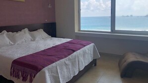 A bedroom with a large bed, a window with a view of the sea, and a painting on the wall. - Amara Ixtapa, Luxury Oceanfront Condo, 6th Floor (Ixtapa)