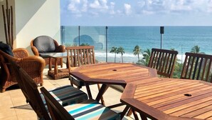 A wooden table and chairs on a balcony with a view of the ocean and palm trees. - Amara Ixtapa, Luxury Oceanfront Condo, 6th Floor (Ixtapa)