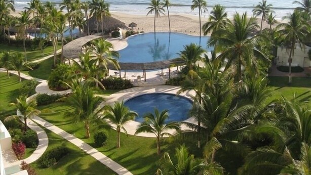A resort with a large pool, palm trees, and a beach view. - Amara Ixtapa, Luxury Oceanfront Condo, 6th Floor (Ixtapa)