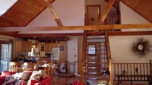 A spacious loft with a high ceiling, wooden beams, a kitchen area, and a dining space with red cushions. - Lakefront home with something to enjoy for every season! (Lee)