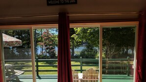 A room with a large sliding glass door leading to an outdoor deck with a green railing, a wooden bench, and a picnic table. - Lakefront home with something to enjoy for every season! (Lee)