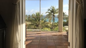 Une pièce dotée d’une grande porte-fenêtre coulissante donnant sur un balcon avec vue sur l’océan et les palmiers.
