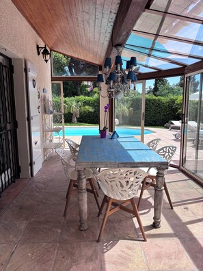 Eine überdachte Terrasse mit Tisch und Stühlen, ein Pool und Blick auf Grünflächen.