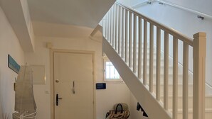 Eine Treppe mit weißen Geländern führt zu einer erhöhten Ebene, eine Tür mit Griff, ein Stuhl mit einer Tasche und ein Tisch mit einem dekorativen Gegenstand.