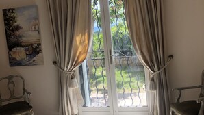 Ein Schlafzimmer mit einem Bett, zwei Stühlen, einem Gemälde und einer Glastür mit Vorhängen.