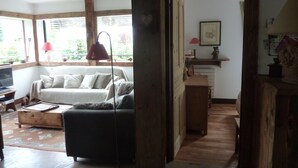 A cozy living room with a sofa, a wooden coffee table, and a TV. There is a wooden door leading to another room.