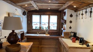 A rustic kitchen with wooden cabinetry, a large window with decorative window treatments, and various kitchen appliances.