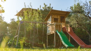 Une cabane en bois avec un toboggan et des balançoires, installée dans un espace herbeux.