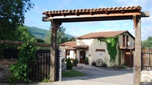 Un bâtiment rustique avec un toit en tuiles, une entrée agrémentée d’une pergola en bois et un mur en pierre.