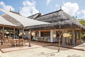 Relax in a shaded outdoor space with a thatched-roof structure, comfortable seating, and decorative lighting.