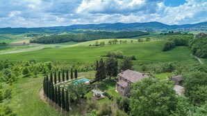 Paisaje rural con una casa de piedra, una piscina y un césped bien cuidado.