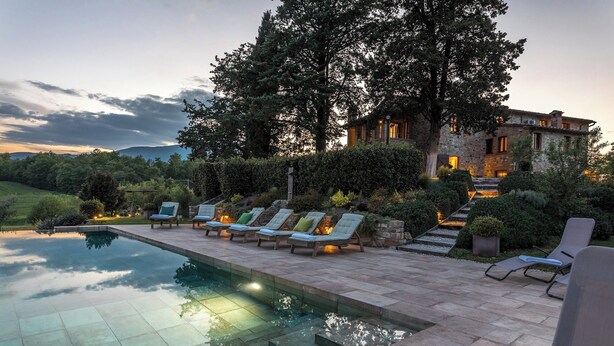 Zona junto a la piscina con sillones de descanso y un edificio de piedra al fondo.