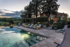 Ein Poolbereich mit Liegestühlen und einem dahinterliegenden Steinhaus.