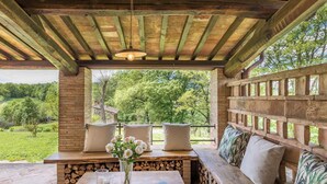 Un banco de madera con cojines, una mesa con un jarrón de flores y vistas a un paisaje verde.