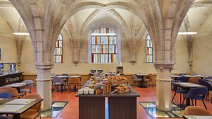 Una biblioteca espaciosa con altos techos abovedados y amplias ventanas. Se disponen mesas y sillas para lectura y estudio.
