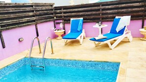 Un espace piscine aménagé sur le toit, comprenant une petite piscine, deux chaises longues et une pergola en bois.