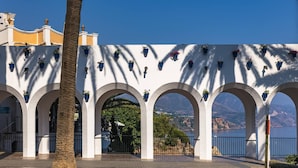 Un bâtiment blanc doté de nombreuses arcades, agrémenté de plantes en pot et offrant une vue sur un paysage montagneux.
