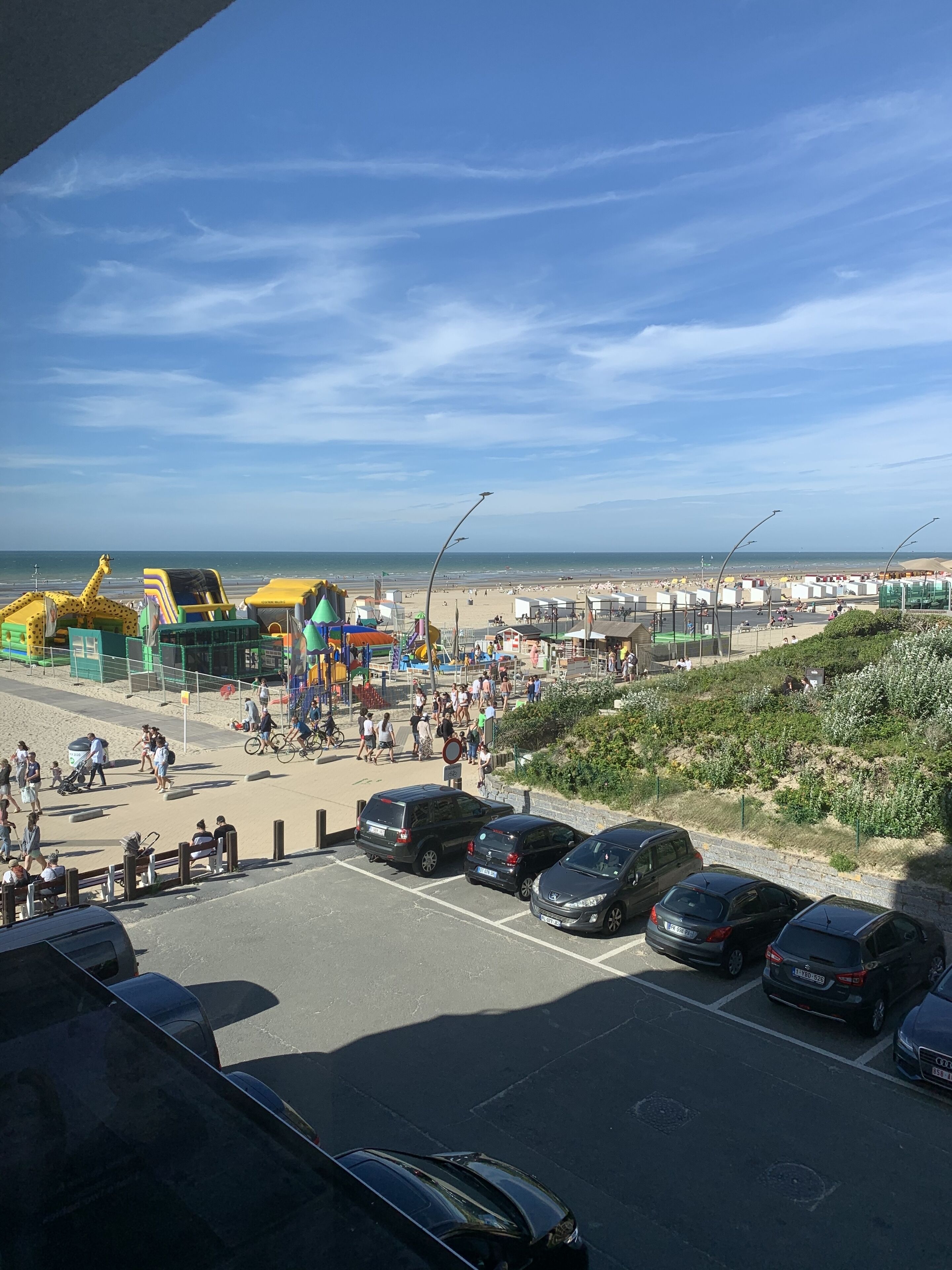 A beachside parking area with cars, a pedestrian walkway, and beach umbrellas.