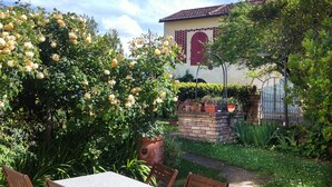 A garden with a table and chairs, a brick wall, and a building with a red door and window. - Lovely Barn with Private Poolnear San Gimignano, between Florence and Siena. (Castelfiorentino)