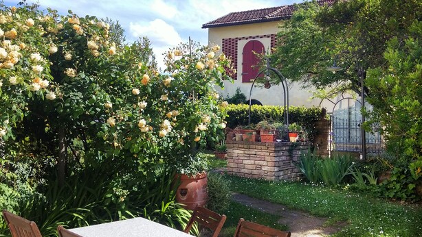 Un jardin avec une table et des chaises, un mur de briques et un bâtiment avec une porte et une fenêtre rouges.