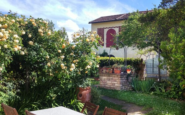 A garden with a table and chairs, a brick wall, and a building with a red door and window. - Lovely Barn with Private Poolnear San Gimignano, between Florence and Siena. (Castelfiorentino)