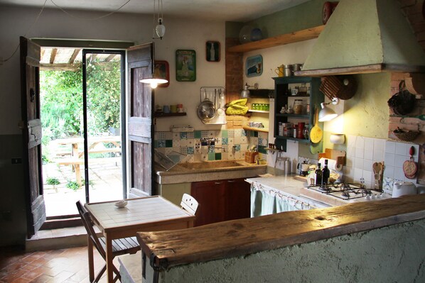 Een keuken met een houten tafel, een gasfornuis en diverse keukenspullen op planken.
