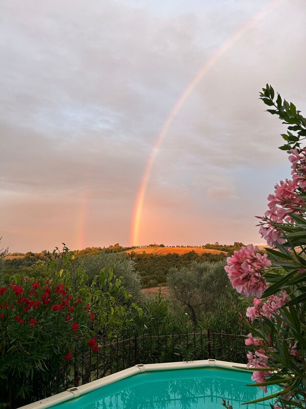 A swimming pool with a view of a rainbow over a hilly landscape.
