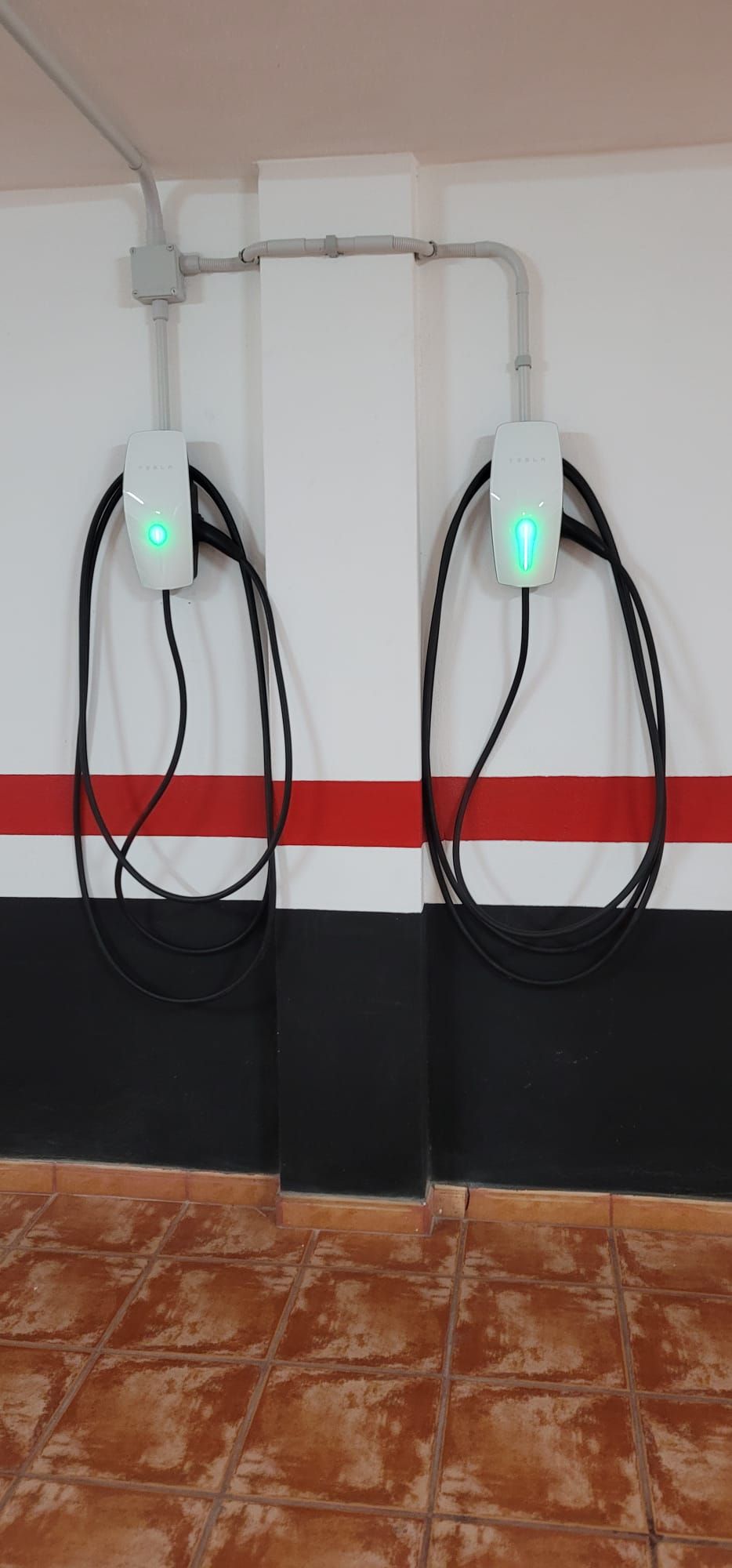 Two wall-mounted electrical outlets with green lights, connected by a white cable.