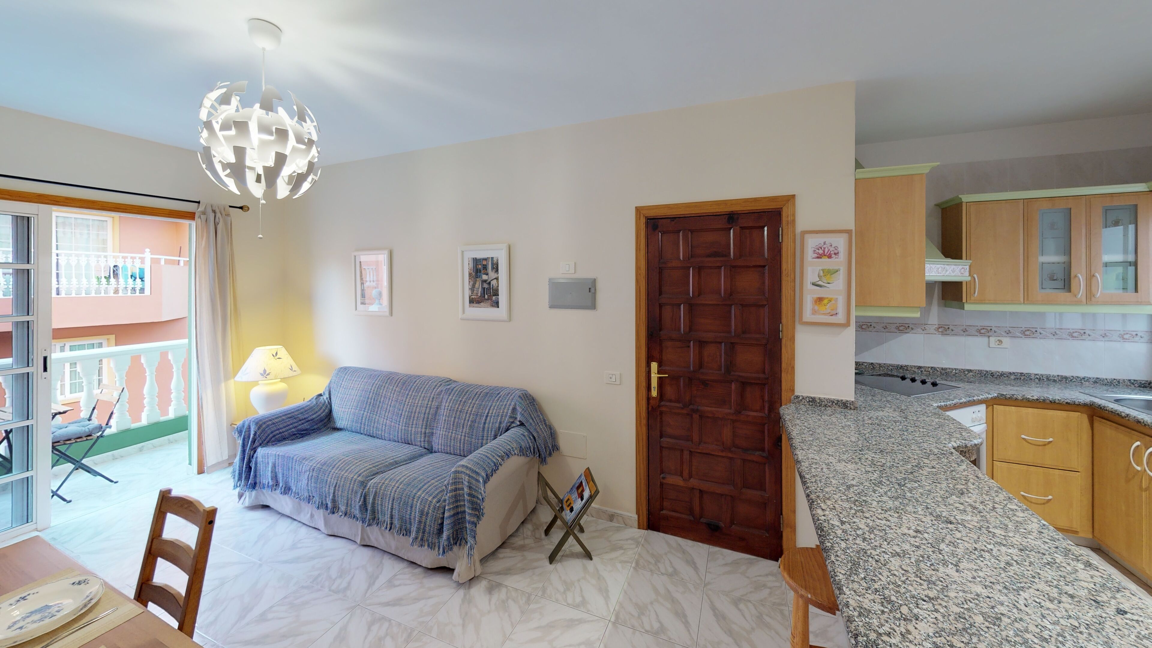 Ein Wohnzimmer mit einer Couch, einem Esstisch mit Stühlen, einer Holztür und einer Küchenzeile mit Schränken und Arbeitsplatte.