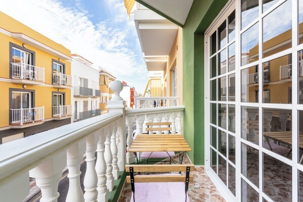 A balcony with a wooden table and chairs, white balustrades, and a view of neighboring buildings.