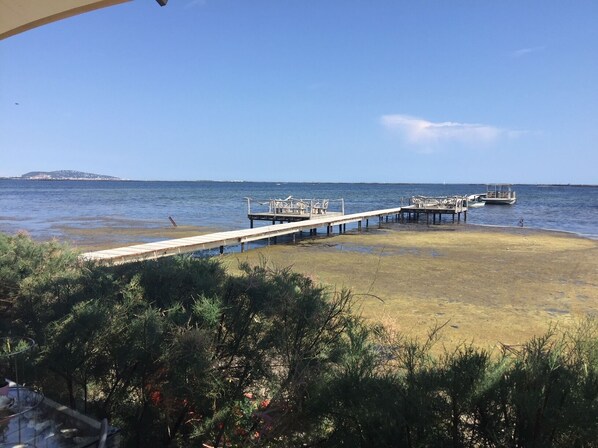 A beach with a wooden pier extending into the water, a boat docked at the end, and a distant island. - Contemporary upscale villa, heated pool with jacuzzi. Breathtaking view (Pézenas)