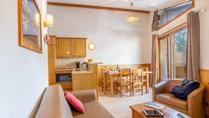 Ein gemütliches Wohnzimmer mit Sofa und Sessel, ein Essbereich mit Tisch und Stühlen, eine Küche mit Holdekor und einer Mikrowelle, sowie große Fenster mit Vorhängen.