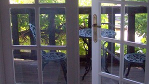 Une porte en bois, dotée de plusieurs panneaux de verre, qui donne sur une terrasse extérieure avec des tables et des chaises en métal.