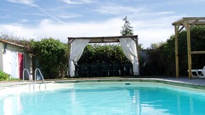 Une piscine d’eau cristalline, avec une pergola en bois et des chaises en arrière-plan.