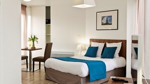 A hotel room with a bed, a desk, a chair, a lamp, and a painting on the wall. - Studio spacieux, près monuments historiques (Amiens)