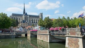 A historic building with Gothic architecture, a canal with a bridge, and a flower-adorned fence. - Studio spacieux, près monuments historiques (Amiens)