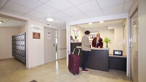 A reception area with a counter, a sign for 'Odalys', a phone, and a plant. - Studio spacieux, près monuments historiques (Amiens)