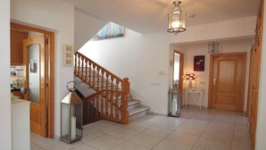 A spacious hallway with a wooden staircase, a small table with a lamp, and a door with a decorative panel. - Beautifully Furnished Family Villa with Spectacular Views and Pool.  (Moriara)