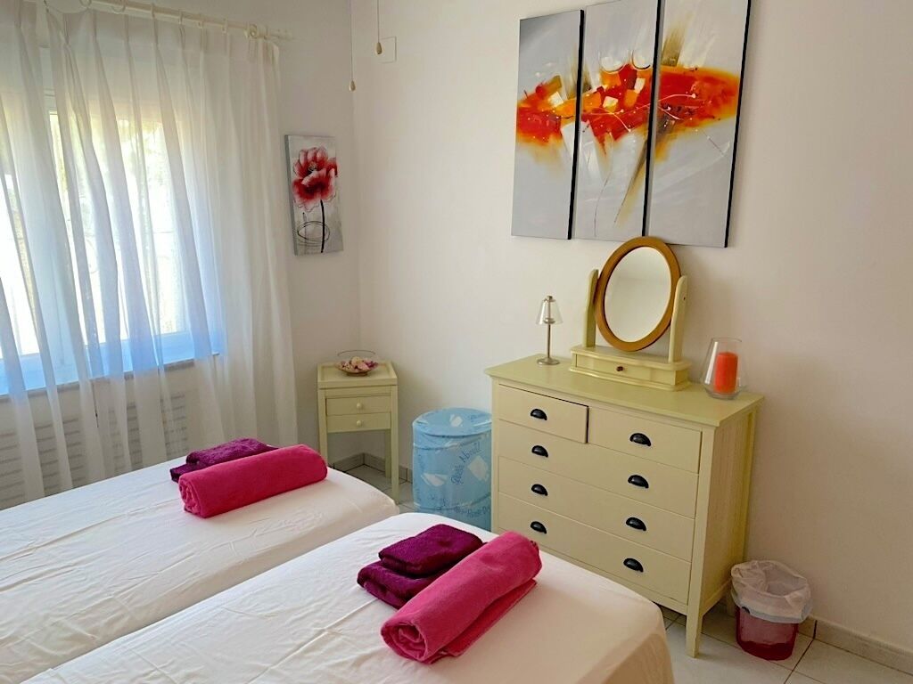 A hotel room with two beds, a bedside table with a lamp, a mirror, and artwork on the wall.
