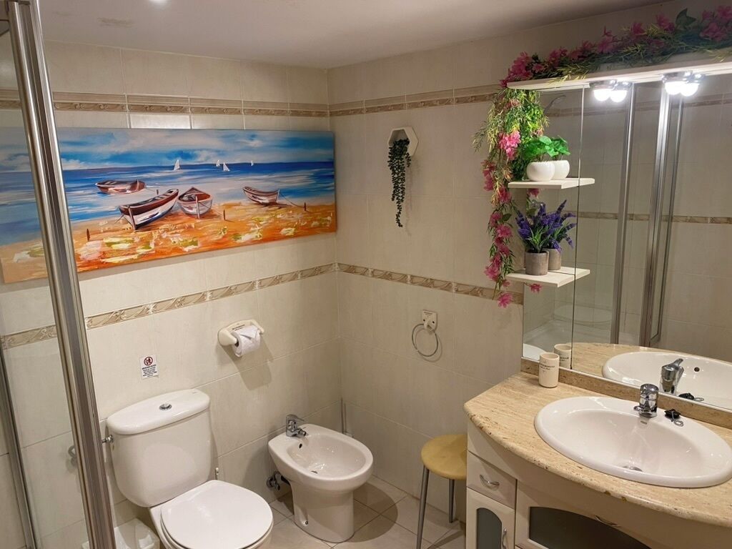 Un baño con un cuadro de barcos en la pared, inodoro, bidé, lavamanos y un espejo.