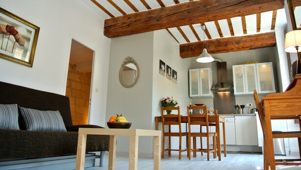 Un salon chaleureux avec un plafond en bois, un coin repas avec une table et des chaises, et une cuisine avec des meubles blancs et une cuisinière.