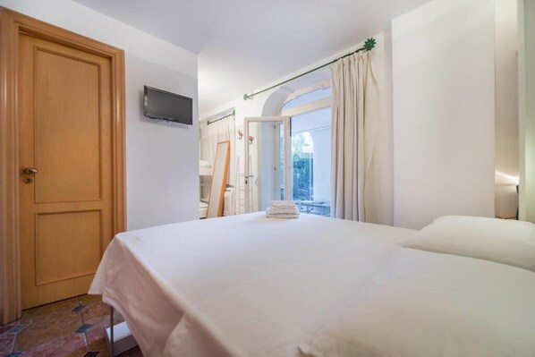 A hotel room with a bed, a television, a door, and a view of the outside.
