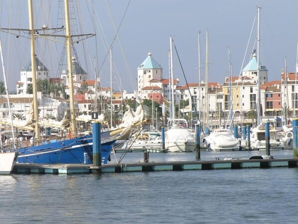 A marina with various boats docked, a building with a green roof, and a clear sky. - Luxury Front Line Apartment with large 60m2 Balcony (Olhos de Agua)