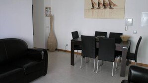 Una sala de estar moderna con comedor, que presenta un jarrón grande, un cuadro de veleros y un sofá de cuero negro.