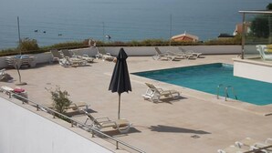 Piscina en la azotea con sillones y una sombrilla, con vistas a una masa de agua.