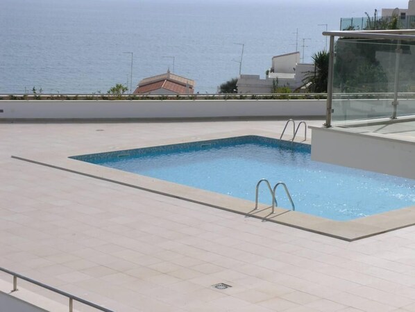 A rectangular swimming pool with metal ladders on one side, surrounded by a tiled deck. - Luxury Front Line Apartment with large 60m2 Balcony (Olhos de Agua)