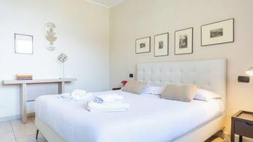A neatly made bed with pillows and folded towels, a bedside table with books, and a wall-mounted picture frame.